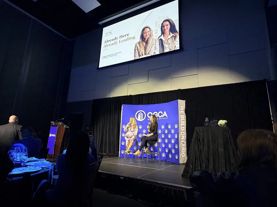 A fireside conversation on the OGCA stage, the talk title on the screen above and the audience in the foreground